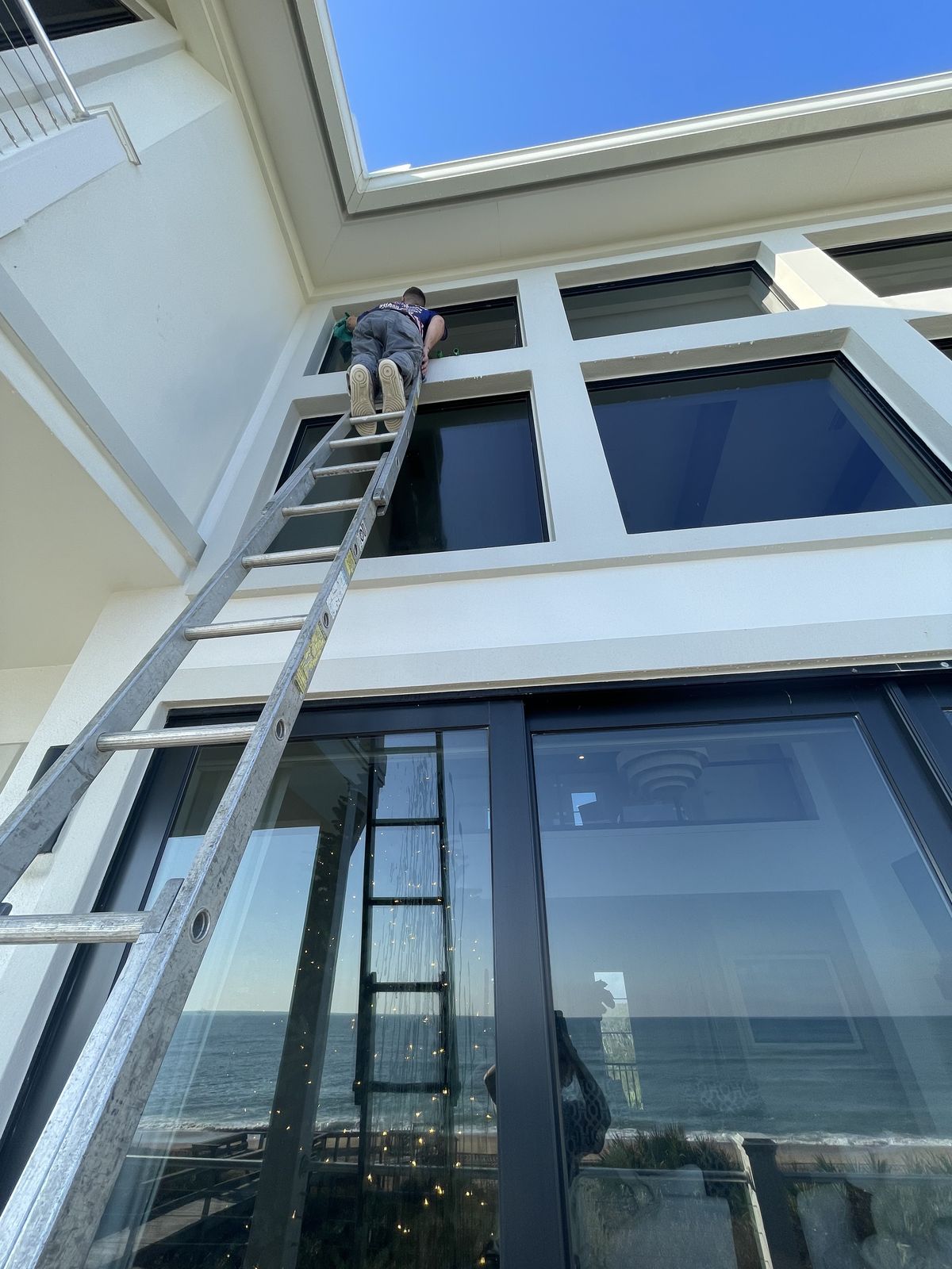 Hospitality Improvements Inc. crew member cleaning tall oceanfront window glass on a ladder near Ponte Vedra Beach FL