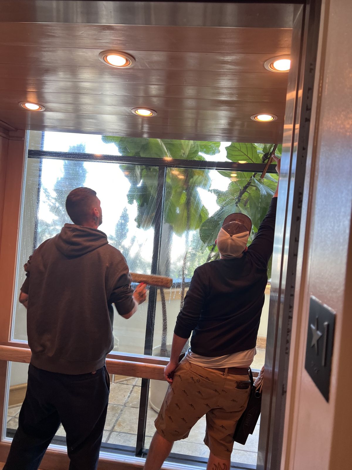 Two Hospitality Improvements Inc. crew members cleaning large glass windows with squeegees in the Jacksonville area